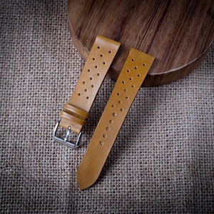 May include: Two brown leather watch straps with a perforated design. The straps are laid out on a brown burlap surface.