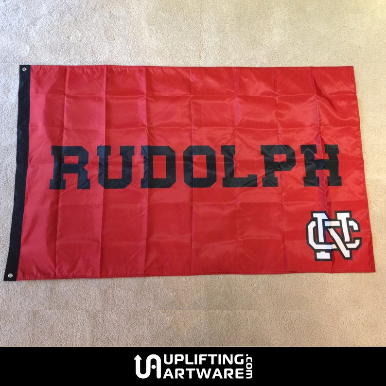 May include: A red flag with the word "RUDOLPH" in black block letters and a white "NC" logo in the bottom right corner.