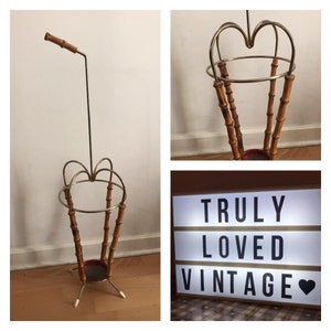 May include: A vintage bamboo and metal umbrella stand with a chrome finish. The stand has a round base and three legs. The stand is designed to hold umbrellas upright.