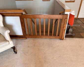 May include: A wooden gate with vertical slats, installed at the top of a staircase. The gate is stained a dark brown color and is closed.