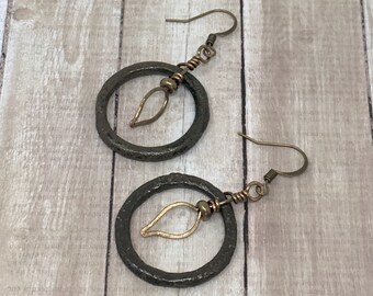 May include: A pair of bronze hoop earrings with a small leaf charm hanging from each hoop.