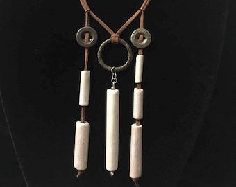May include: A brown suede necklace with three white cylindrical beads and two silver rings. The necklace has a silver circle pendant.