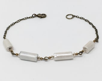 May include: A white beaded bracelet with a bronze chain and clasp. The bracelet features four white cylindrical beads.
