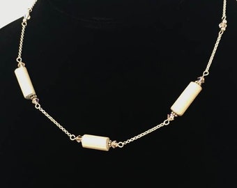 May include: A silver chain necklace with three white cylindrical beads and small crystal accents.