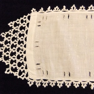 May include: A white linen table runner with a delicate crocheted lace border. The runner has several evenly spaced buttonholes along the edges.