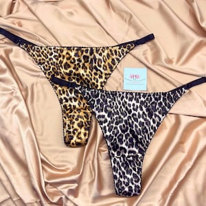 May include: Two pairs of leopard print thongs, one black and white and one brown and gold. The thongs are made of satin and have adjustable straps.