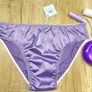 Puede incluir: Un par de ropa interior de color lavanda con ribete blanco. La ropa interior tiene un estampado de lunares y est&aacute; hecha de un material brillante. Suministros de costura, incluyendo tijeras, alfileres e hilo, est&aacute;n junto a la ropa interior.