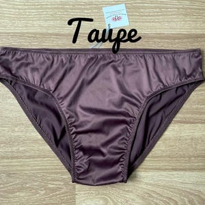 Puede incluir: Bragas color taupe hechas de un material sedoso. La ropa interior tiene un corte cl&aacute;sico y una textura suave y brillante. La palabra "Taupe" est&aacute; escrita en cursiva encima de la ropa interior.