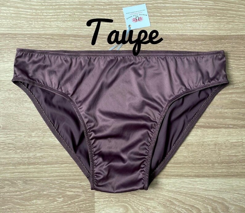 Puede incluir: Bragas color taupe hechas de un material sedoso. La ropa interior tiene un corte cl&aacute;sico y una textura suave y brillante. La palabra "Taupe" est&aacute; escrita en cursiva encima de la ropa interior.