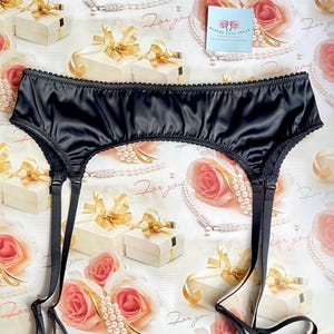May include: Black satin garter belt with adjustable straps and a scalloped edge. The lingerie is displayed on a background with gift boxes, roses, and the text "For you".