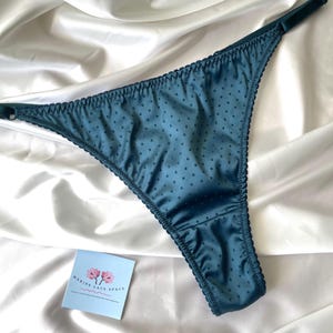 May include: Teal-colored thong underwear with a polka dot pattern. The lingerie has a delicate, scalloped trim and a satin finish. A small card with the text "MARINE LACE SPACE" and a floral design is visible.