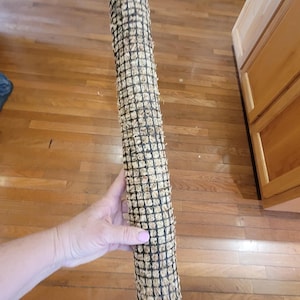 May include: A cylindrical plant support pole, approximately 36 inches long, made of a woven black mesh filled with a fibrous, light brown material. A wooden stake is attached to the bottom. The pole is designed to support climbing plants.