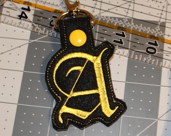 May include: A black felt keychain with a yellow embroidered letter A and a yellow button.
