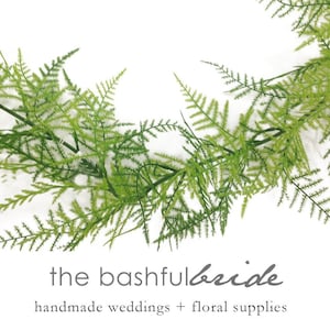 May include: A vibrant green artificial fern garland, perfect for weddings and floral arrangements. The garland is arranged in a semi-circle against a white background. The text "the bashful bride" and "handmade weddings + floral supplies" is visible.
