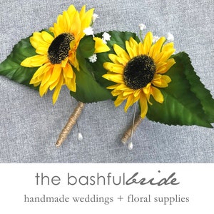 May include: Two yellow sunflower boutonnieres with green leaves and white baby's breath. The stems are wrapped in twine and have pearl accents. "the bashful bride" is written in cursive below the image. "handmade weddings + floral supplies" is written below the cursive text.