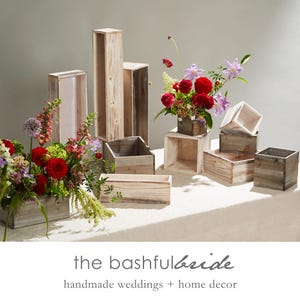 May include: A collection of various sized, unfinished wooden boxes and pedestals, some holding vibrant floral arrangements with red, purple, and green blooms. The text "the bashful bride" and "handmade weddings + home decor" is visible.