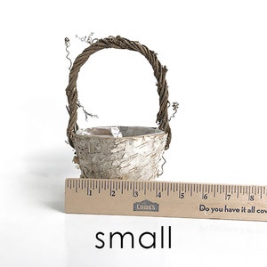 May include: A small, white birch bark basket with a brown twig handle. The basket is about 4 inches tall and 3 inches wide. A ruler is in the image for scale.
