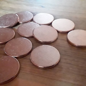 Può includere: Una collezione di 11 ombretti rotondi, metallici, color oro rosa. Gli ombretti sono disposti in un cerchio sciolto su una superficie di legno.