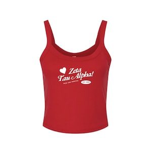 May include: A red tank top with a scoop neck and spaghetti straps. The white text on the front says "Zeta Tau Alpha!" with a heart symbol and the words "Seek the Noblest" and "EST. 1898".