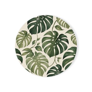 May include: A circular wall art piece featuring a repeating pattern of dark green monstera leaves on a light cream background. The design showcases various sizes of split-leaf philodendron foliage arranged in a dense, overlapping botanical layout.