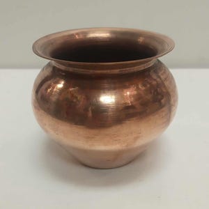 May include: A small, copper pot with a rounded body and a flared rim. The pot has a shiny, polished finish.