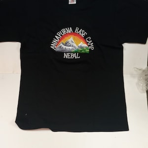May include: Black t-shirt with an embroidered design of mountains and a sunset. The design says "Annapurna Base Camp Nepal".