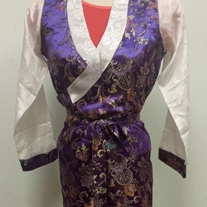 May include: A purple and white robe with a floral pattern and a white collar. The robe has a sash that ties at the waist.
