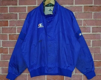 May include: A blue Champion jacket with a white logo and a black zipper. The jacket has a plaid lining and a ribbed hem and cuffs.