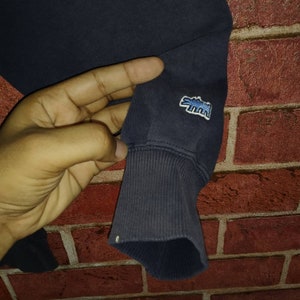 May include: Close-up of a navy blue sweatshirt with a blue and white alligator logo on the sleeve.