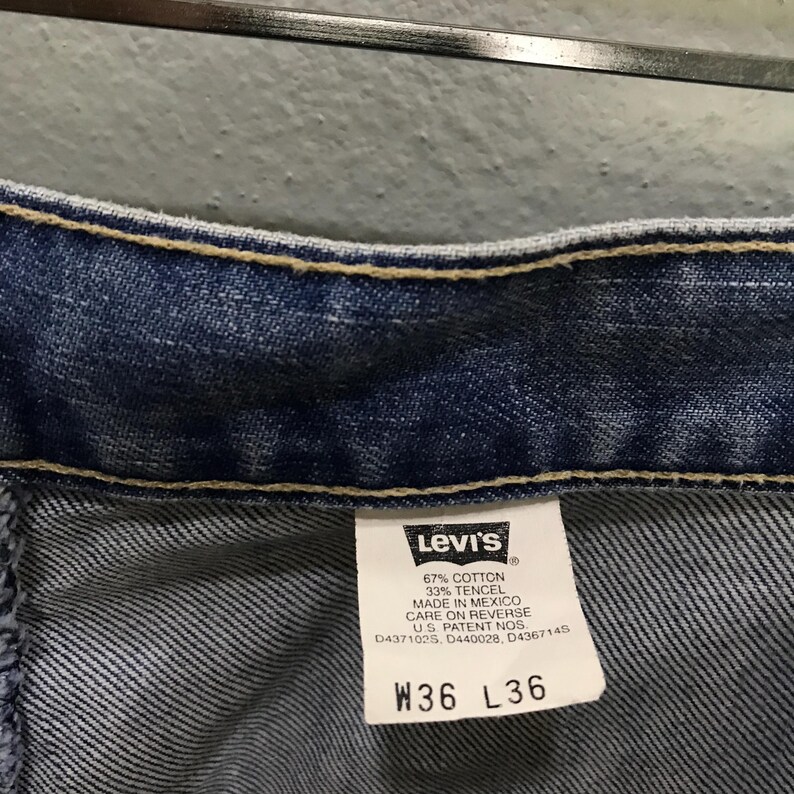 May include: Blue denim jeans featuring a white interior tag with the Levi's logo, fabric composition of 67% cotton and 33% tencel, origin marked as Mexico, and size specifications W36 L36. The garment includes U.S. patent numbers D437102S, D440028, D436714S.