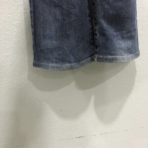 Pu&ograve; includere: Primo piano dell'orlo di un paio di jeans blu. I jeans sono di un lavaggio medio con un aspetto leggermente sbiadito. L'orlo &egrave; cucito con cura con un filo chiaro e il tessuto mostra una sottile usura.