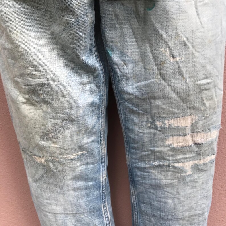 May include: Light blue denim jeans with distressed details, including patches and faded areas. The jeans have a classic five-pocket design and a straight leg cut. The fabric shows signs of wear and tear, giving them a vintage look.
