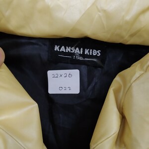 May include: A black label with the text "KANSAI KIDS" and "150" on a yellow jacket. A white tag with the text "22x26" and "022" is attached to the jacket.