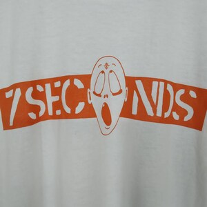 May include: White t-shirt with an orange graphic of a screaming face and the text "7 Seconds".