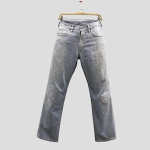 May include: Light grey denim jeans hanging on a wooden hanger. The jeans have a classic five-pocket design, a button and zip closure, and a distressed look with a small tear on the right leg.