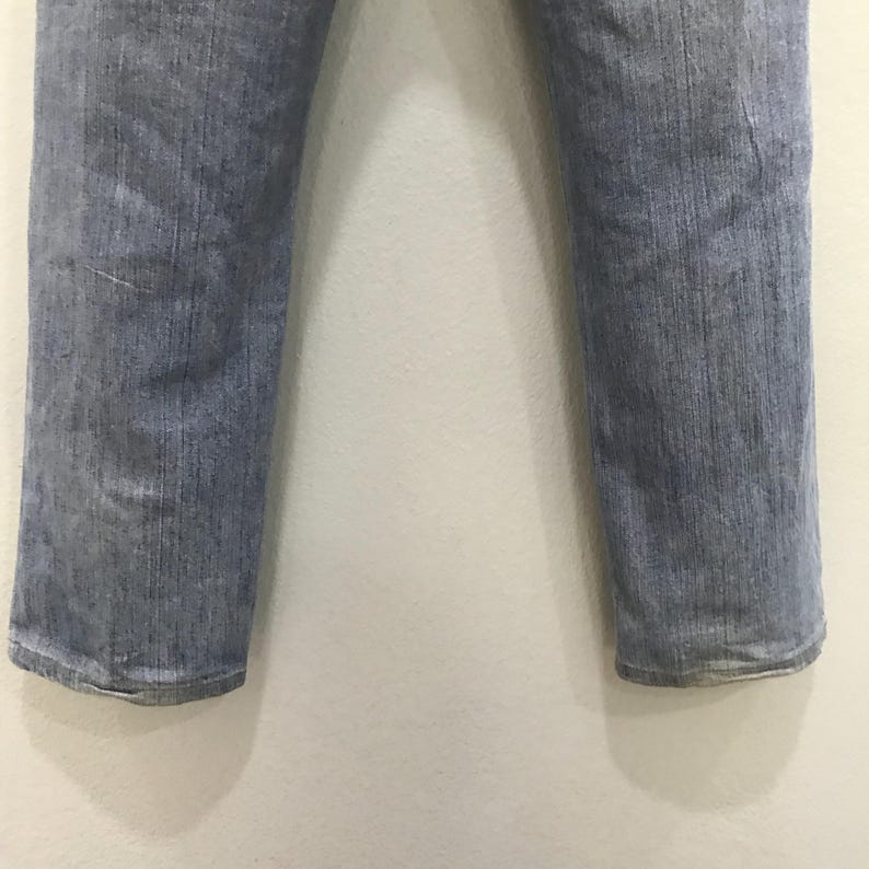 May include: Light blue denim jeans with a straight leg cut. The jeans show signs of wear and fading, with a classic five-pocket design. The image shows the lower portion of the jeans against a plain white background.