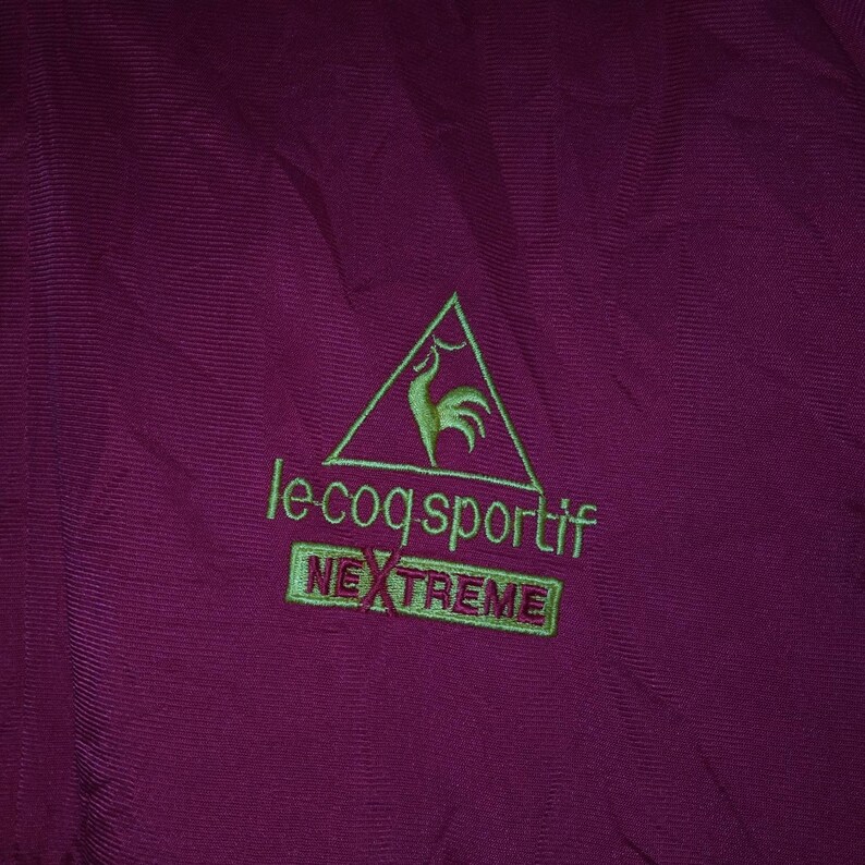 Puede incluir: Una chaqueta color burdeos con un logotipo bordado en verde que dice "le coq sportif" y "NEXTREME" en un rect&aacute;ngulo.