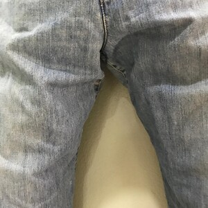 May include: A pair of light blue denim jeans featuring a classic five-pocket construction, a visible center front seam, and a textured fabric finish. The denim displays a faded wash with subtle whiskering patterns along the upper thigh area.