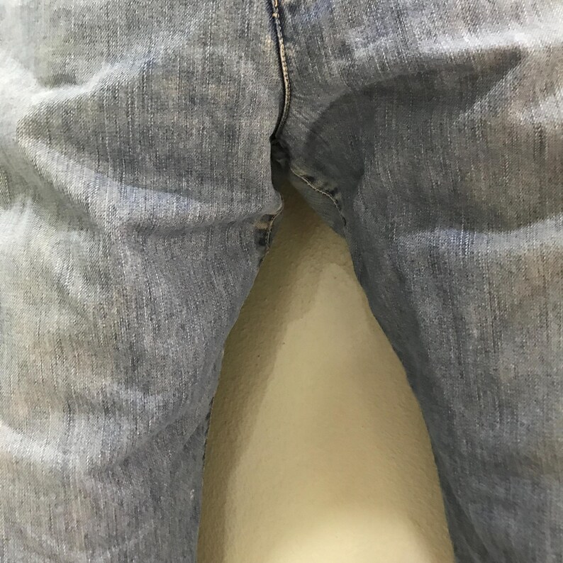 May include: A pair of light blue denim jeans featuring a classic five-pocket construction, a visible center front seam, and a textured fabric finish. The denim displays a faded wash with subtle whiskering patterns along the upper thigh area.