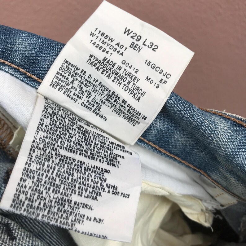 May include: Close-up of denim jeans with tags. The tags display the size W29 L32, along with other details. The text on the tags includes "MADE IN TURKEY" and washing instructions. The jeans are a light blue wash.