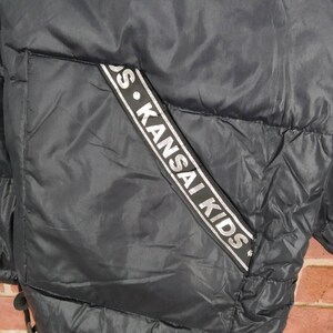 May include: Black puffer jacket with a silver and black logo that reads "S. KANSAI KIDS" on the side.