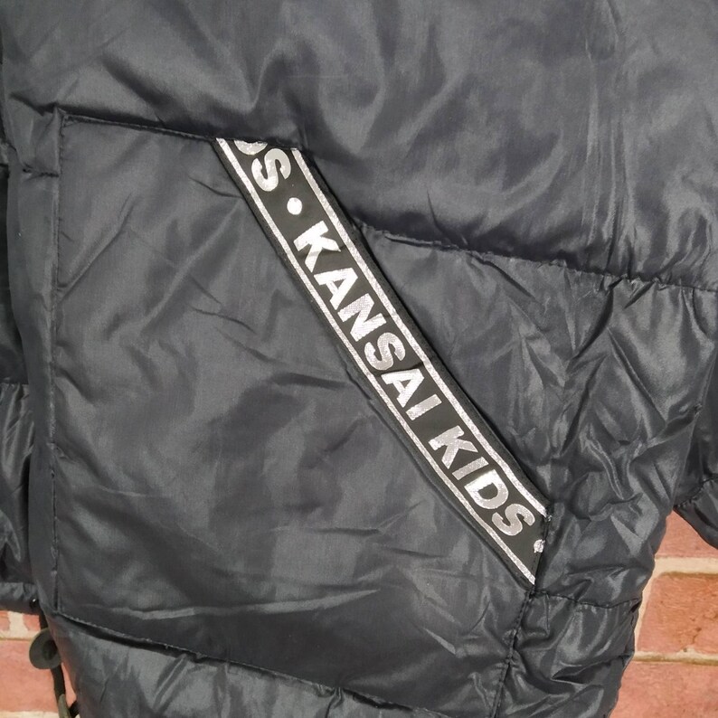 May include: Black puffer jacket with a silver and black logo that reads "S. KANSAI KIDS" on the side.