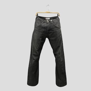 Peut inclure: Un pantalon en jean gris anthracite foncé suspendu à un cintre en métal doré. Le jean présente une taille haute avec une fermeture à boutons, des poches avant incurvées et des jambes larges qui se resserrent légèrement vers l'ourlet inférieur.