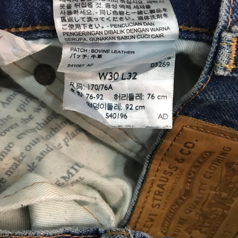 May include: Close-up of a pair of blue denim jeans with a white tag. The tag displays the size W30 L32, measurements in cm, and the text "BOVINE LEATHER". A brown leather patch with "LEVI STRAUSS & CO." is also visible.