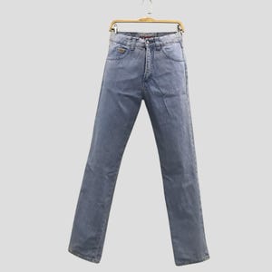 May include: Light blue denim jeans hanging on a wooden hanger. The jeans have a classic five-pocket design, a button and zipper closure, and a straight leg fit. The jeans are made of a medium-weight denim fabric.