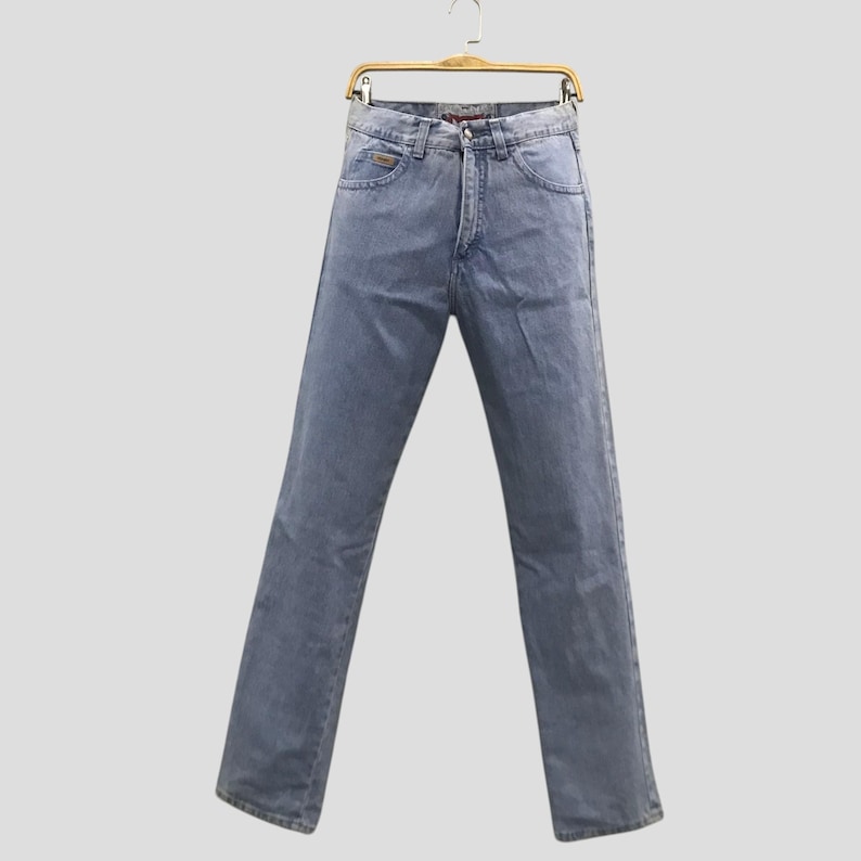 May include: Light blue denim jeans hanging on a wooden hanger. The jeans have a classic five-pocket design, a button and zipper closure, and a straight leg fit. The jeans are made of a medium-weight denim fabric.