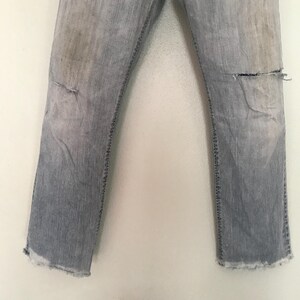 K&ouml;nnte beinhalten: Hellblaue Jeans mit Used-Details, einschlie&szlig;lich Rissen an den Knien und ausgefransten S&auml;umen. Die Jeans weisen Gebrauchsspuren auf, mit verblassten Stellen und Verf&auml;rbungen, was ihnen einen Vintage-Look verleiht.