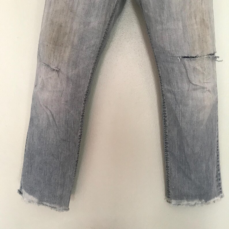 K&ouml;nnte beinhalten: Hellblaue Jeans mit Used-Details, einschlie&szlig;lich Rissen an den Knien und ausgefransten S&auml;umen. Die Jeans weisen Gebrauchsspuren auf, mit verblassten Stellen und Verf&auml;rbungen, was ihnen einen Vintage-Look verleiht.
