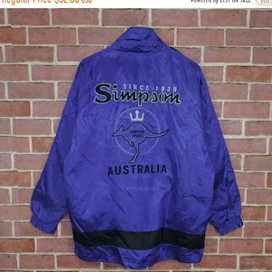 Op de afbeelding: Een paarse windbreaker-jas met een zwarte rits en zwarte bies. De jas heeft een kangoeroe-logo met de tekst "Simpson Sports" en "Australia" op de rug. De tekst "Since 1939" staat boven het logo.