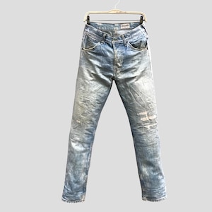 May include: Light blue denim jeans with a faded, distressed appearance. The jeans are hanging on a wooden hanger. The jeans have a classic five-pocket design and a button and zipper closure.